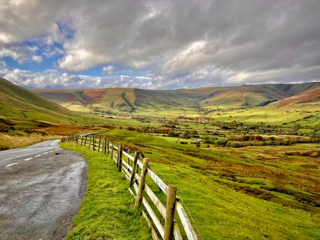 Scenic view of lush green hills and valleys with a winding road and wooden fence, showcasing natural beauty and tranquility