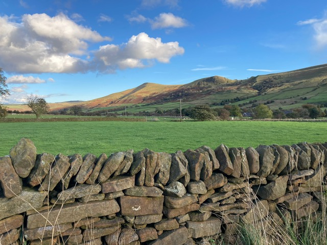 Scenic view of lush green fields and rolling hills with a stone wall in the foreground, showcasing natural beauty
