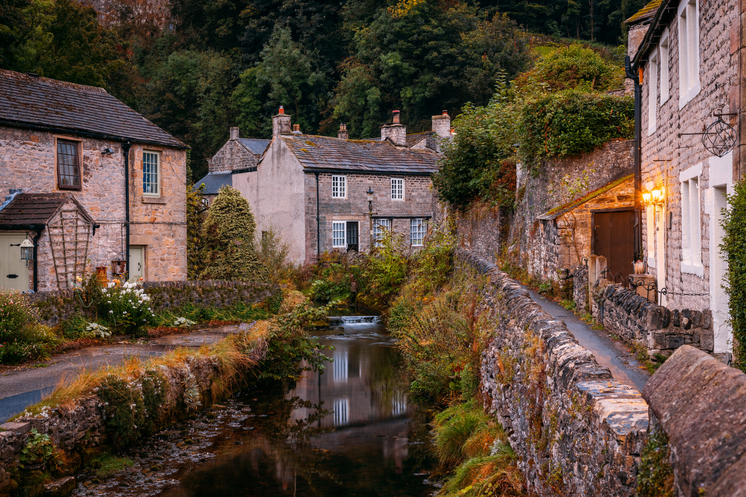 Charming luxury cottage exterior with stone walls, scenic stream, and lush greenery in a tranquil village setting